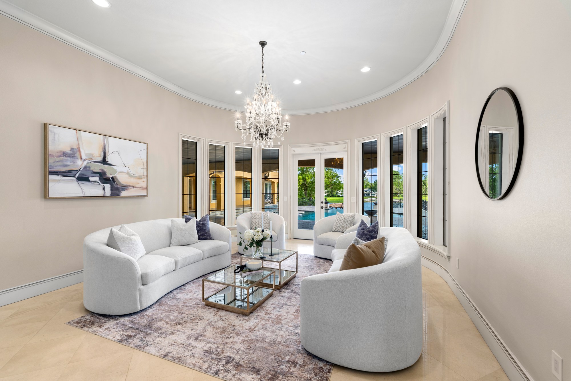 An arched, curved formal living room with a crystal chandelier and French doors to the pool